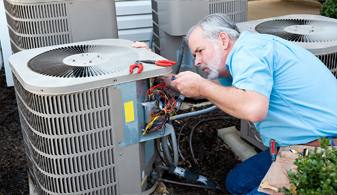 A professional servicing the wiring panel of an outdoor air conditioning condenser unit