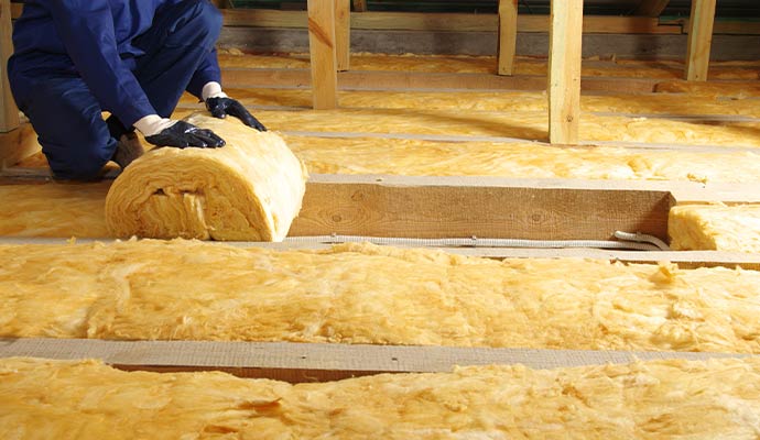 Worker installing fiberglass insulation in attic